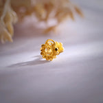 Close-up of a round gold nose pin with beaded border and screw-back fitting on a soft background