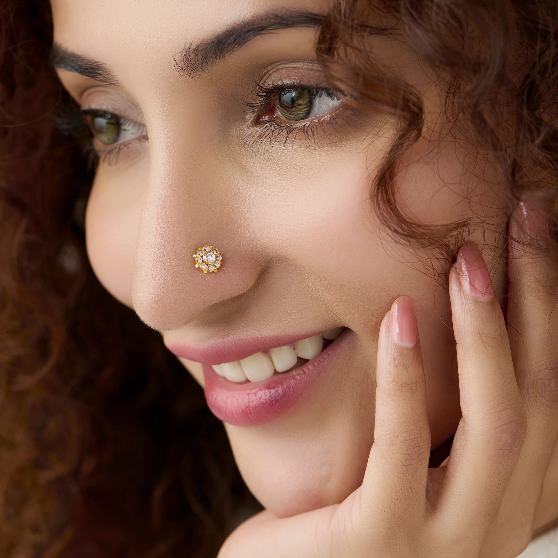 Woman wearing round gold flower nose pin with white center stone