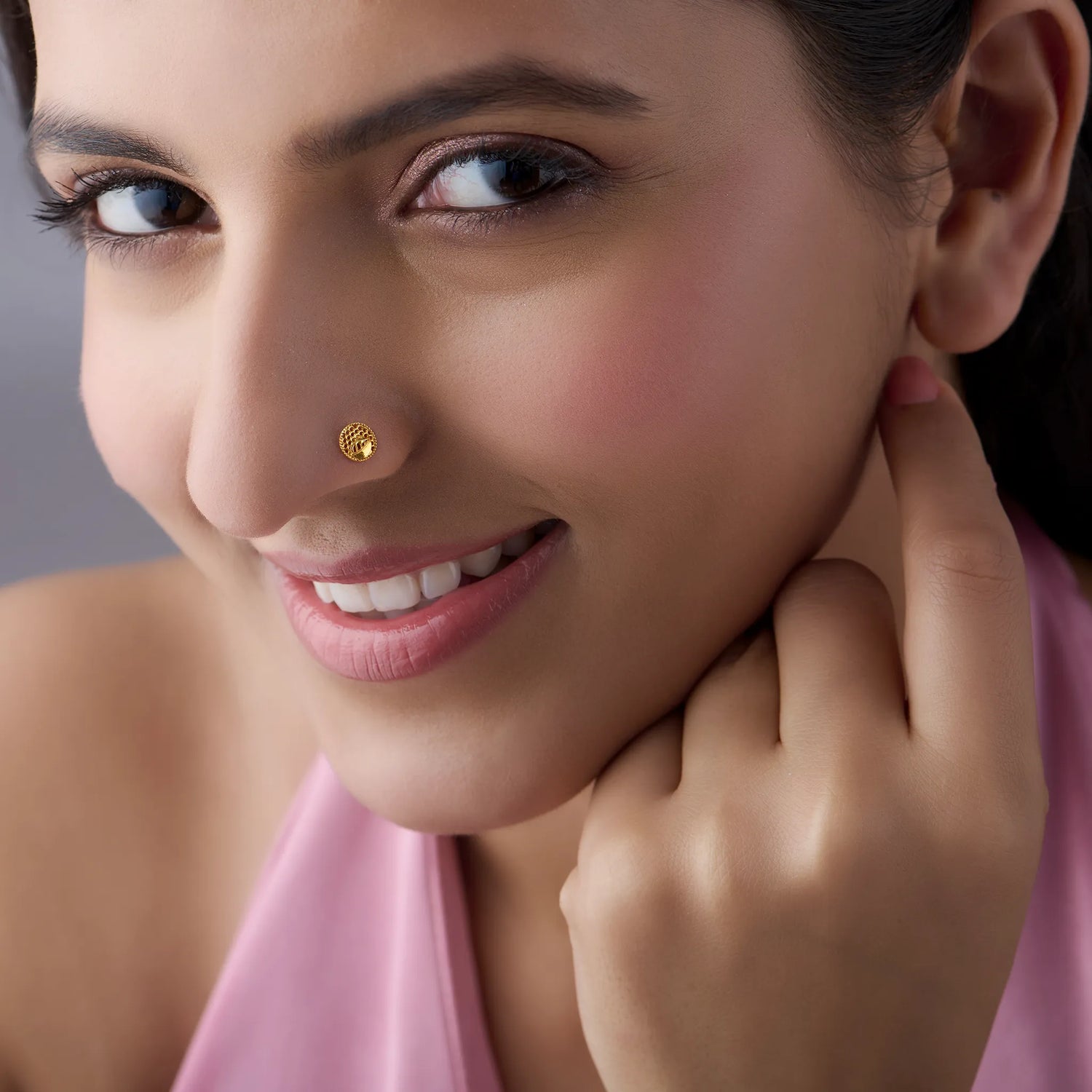 Close-up of a smiling woman wearing a round gold honeycomb-textured nose pin
