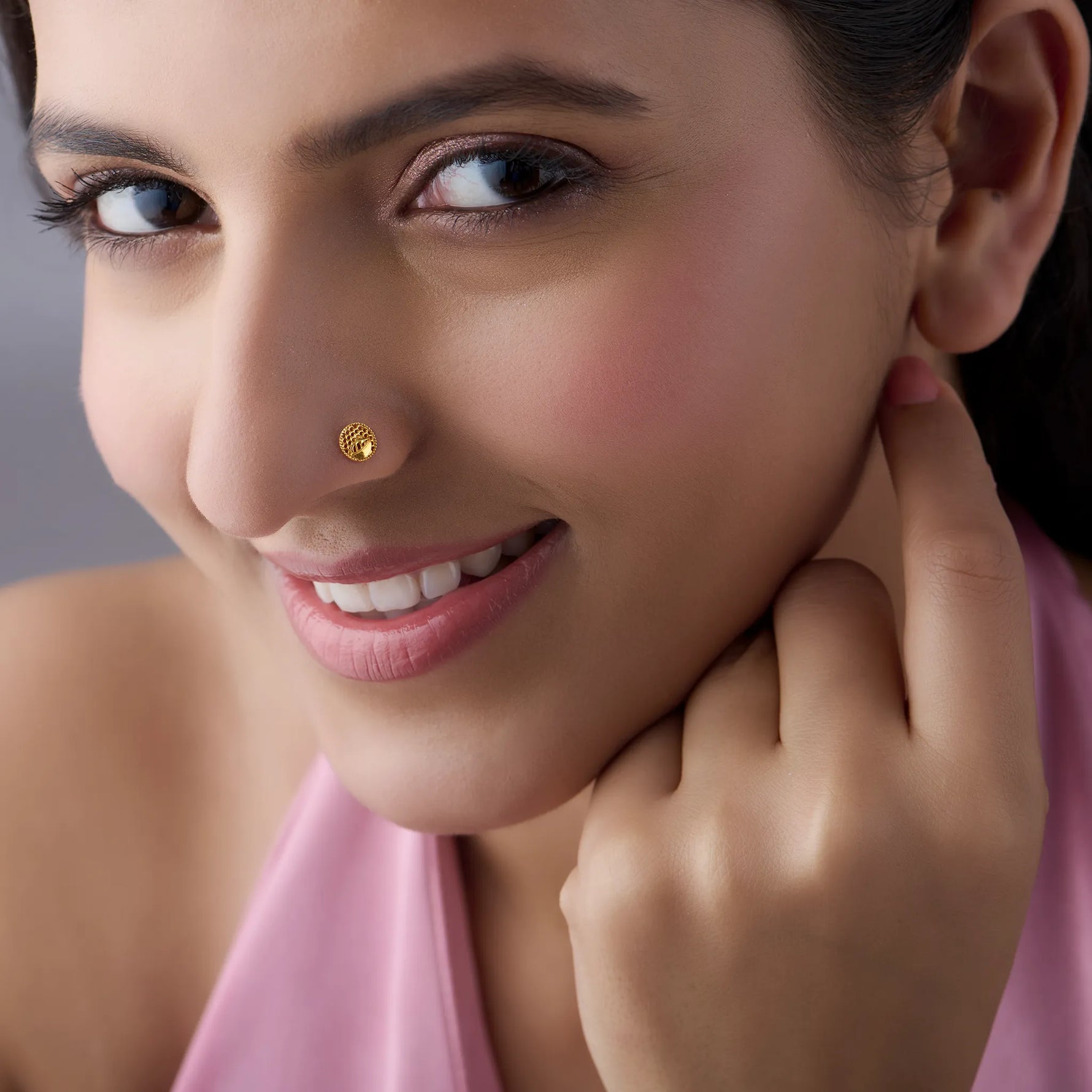 Close-up of a smiling woman wearing a round gold honeycomb-textured nose pin