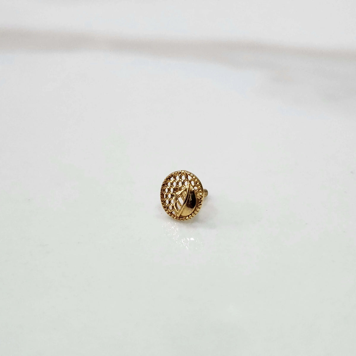 Round gold nose pin with honeycomb pattern and screw-back on a white background