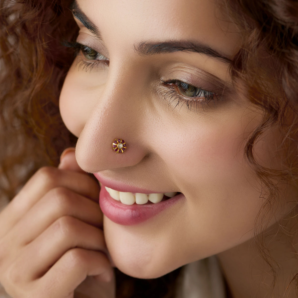 Woman wearing round gold nose pin with maroon and white stones