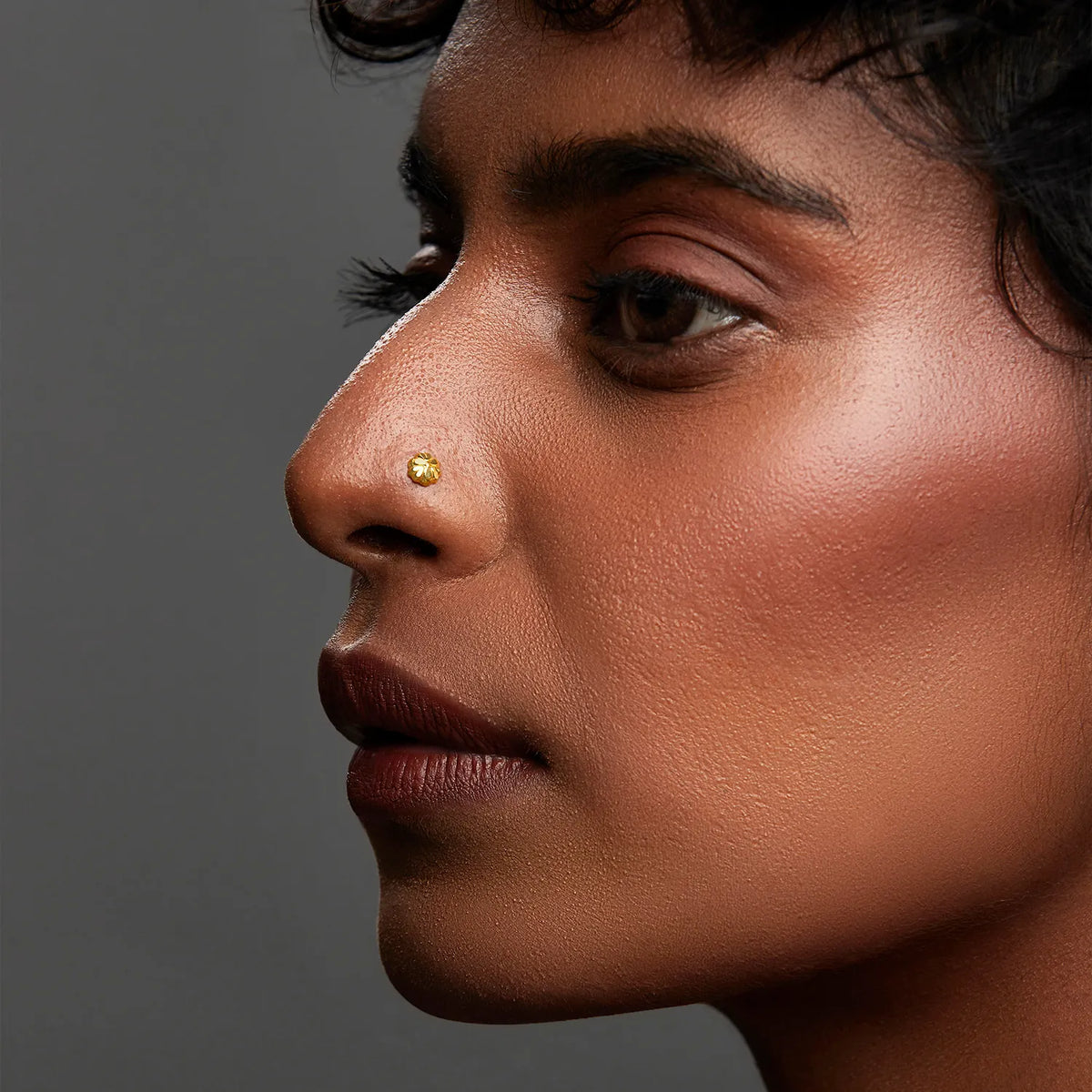 Small round gold nose stud worn on nostril, side profile close-up