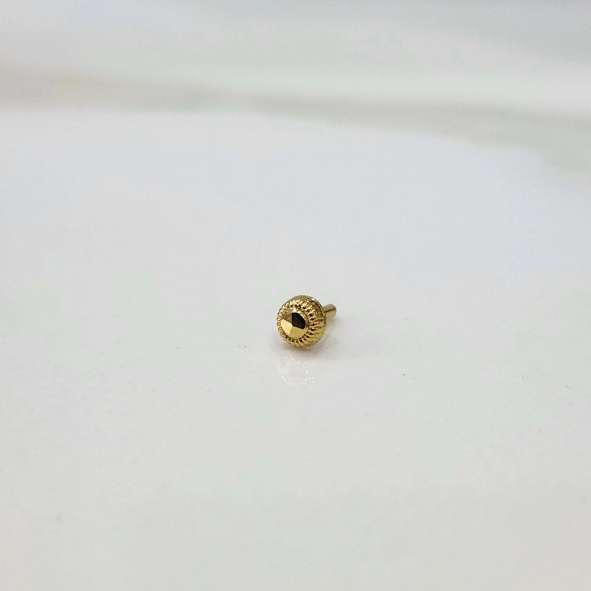Side view of a round gold nose pin with faceted center and screw-back post