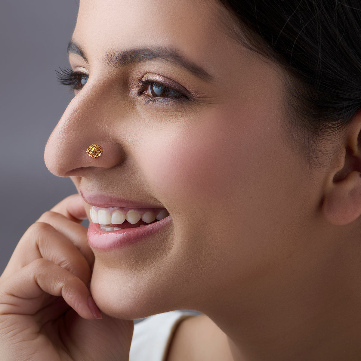 Close-up of a smiling woman wearing a small round textured gold nose pin