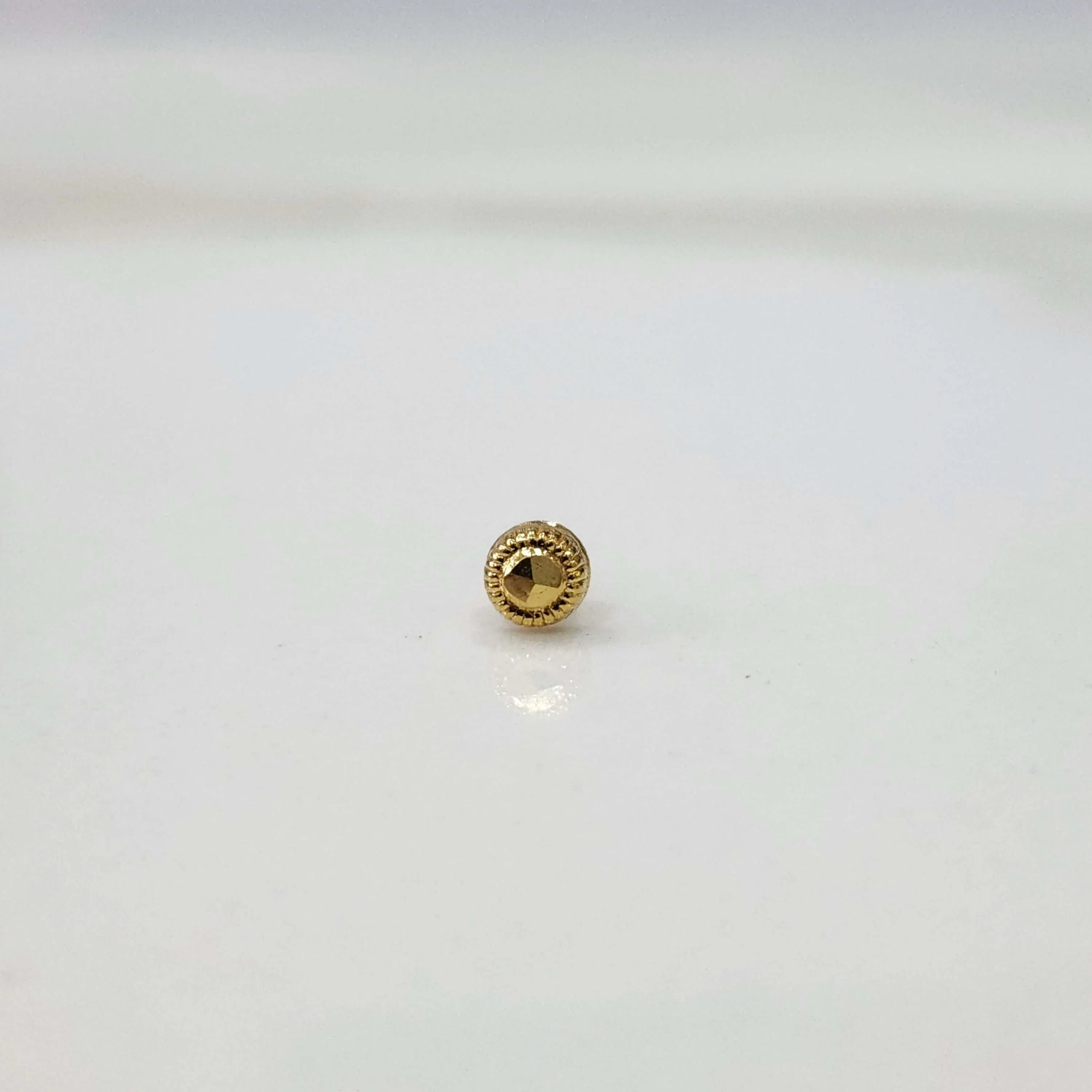 Round gold nose pin with a faceted center and textured border on a white surface