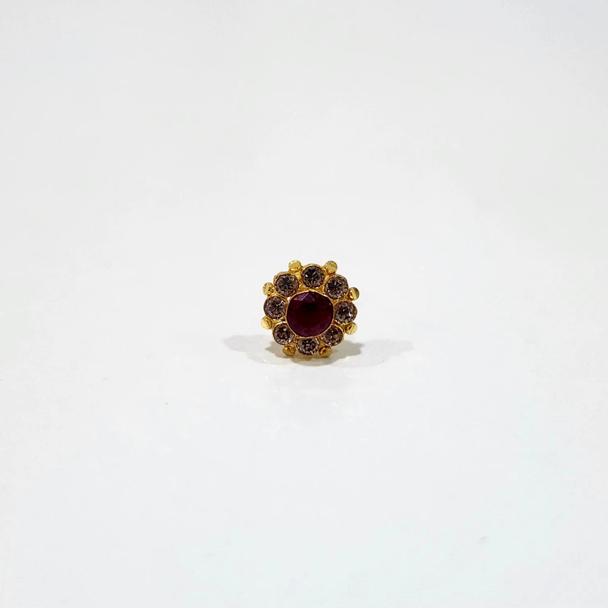 A gold stud earring with a large ruby center stone surrounded by a halo of brown stones, placed on a white background