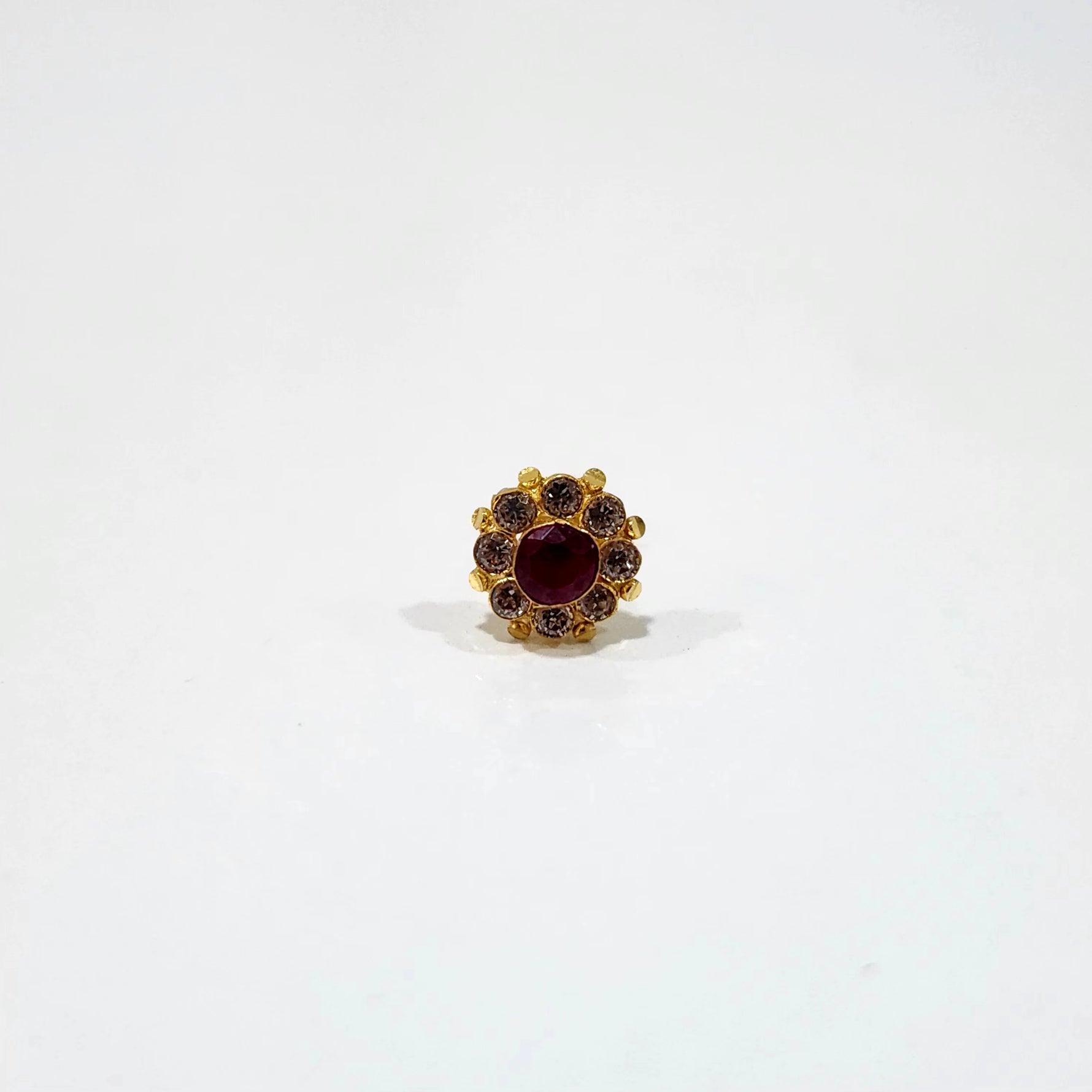 A gold stud earring with a large ruby center stone surrounded by a halo of brown stones, placed on a white background