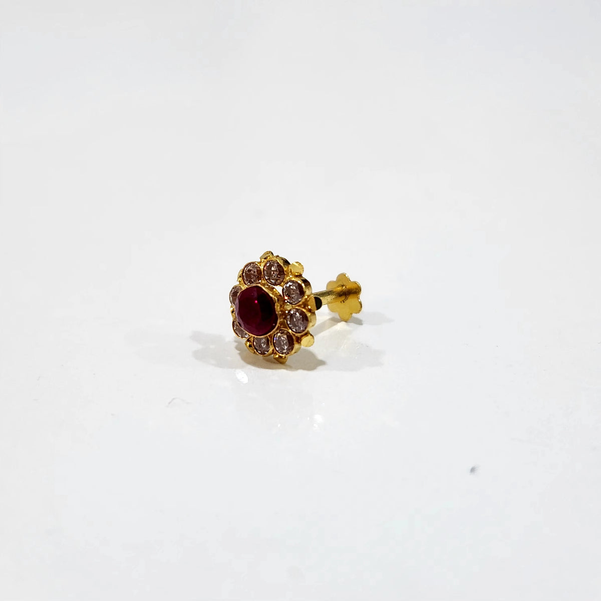 A gold stud earring with a deep ruby center stone framed by a ring of champagne-colored stones and crown-like gold tips, placed on a plain white background
