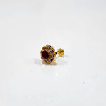 A gold stud earring with a deep ruby center stone framed by a ring of champagne-colored stones and crown-like gold tips, placed on a plain white background