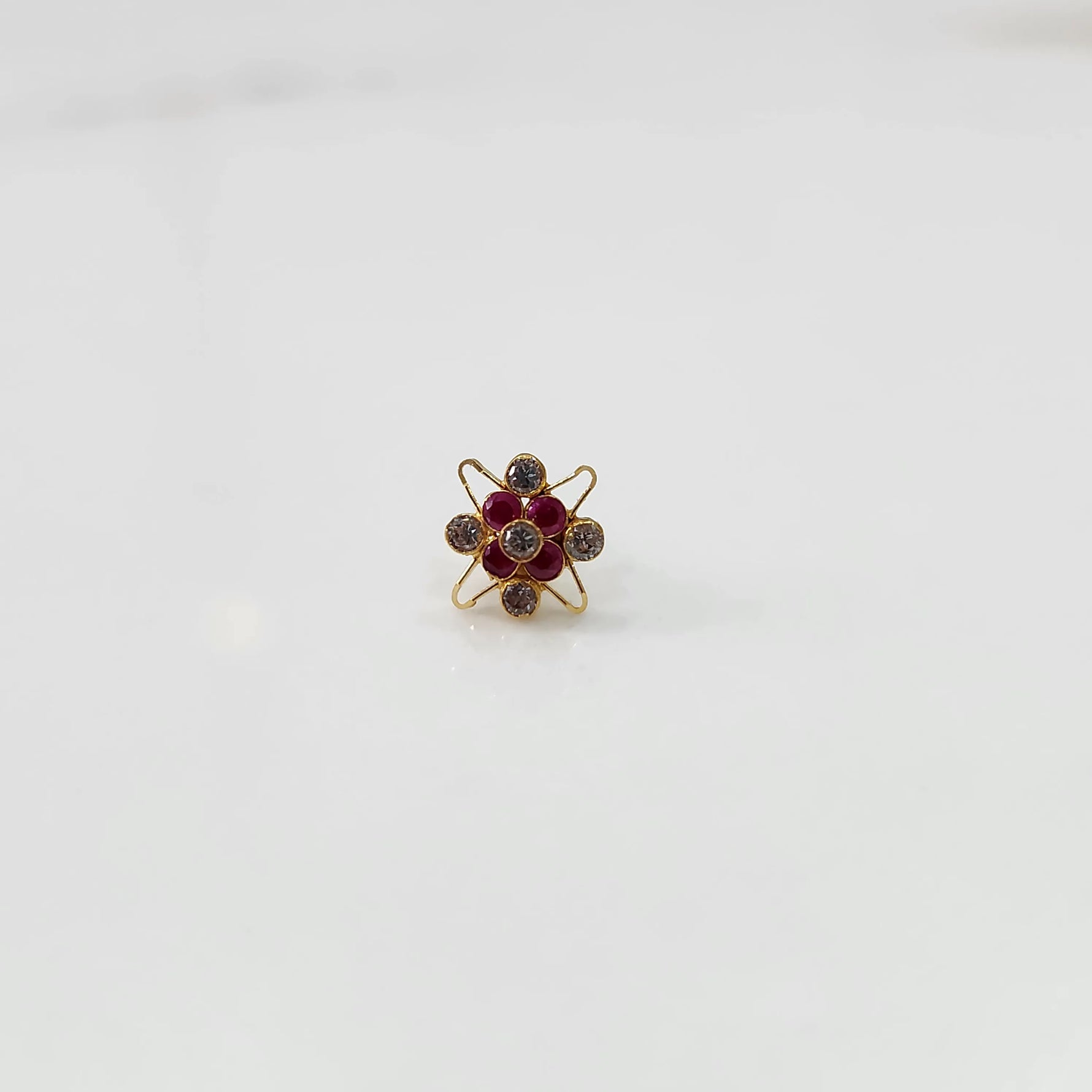 Top view of gold cocktail ring with red ruby and clear stones in flower design
