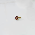 A gold flower-shaped nose pin with ruby stones around a small champagne-colored center stone, placed on a white background
