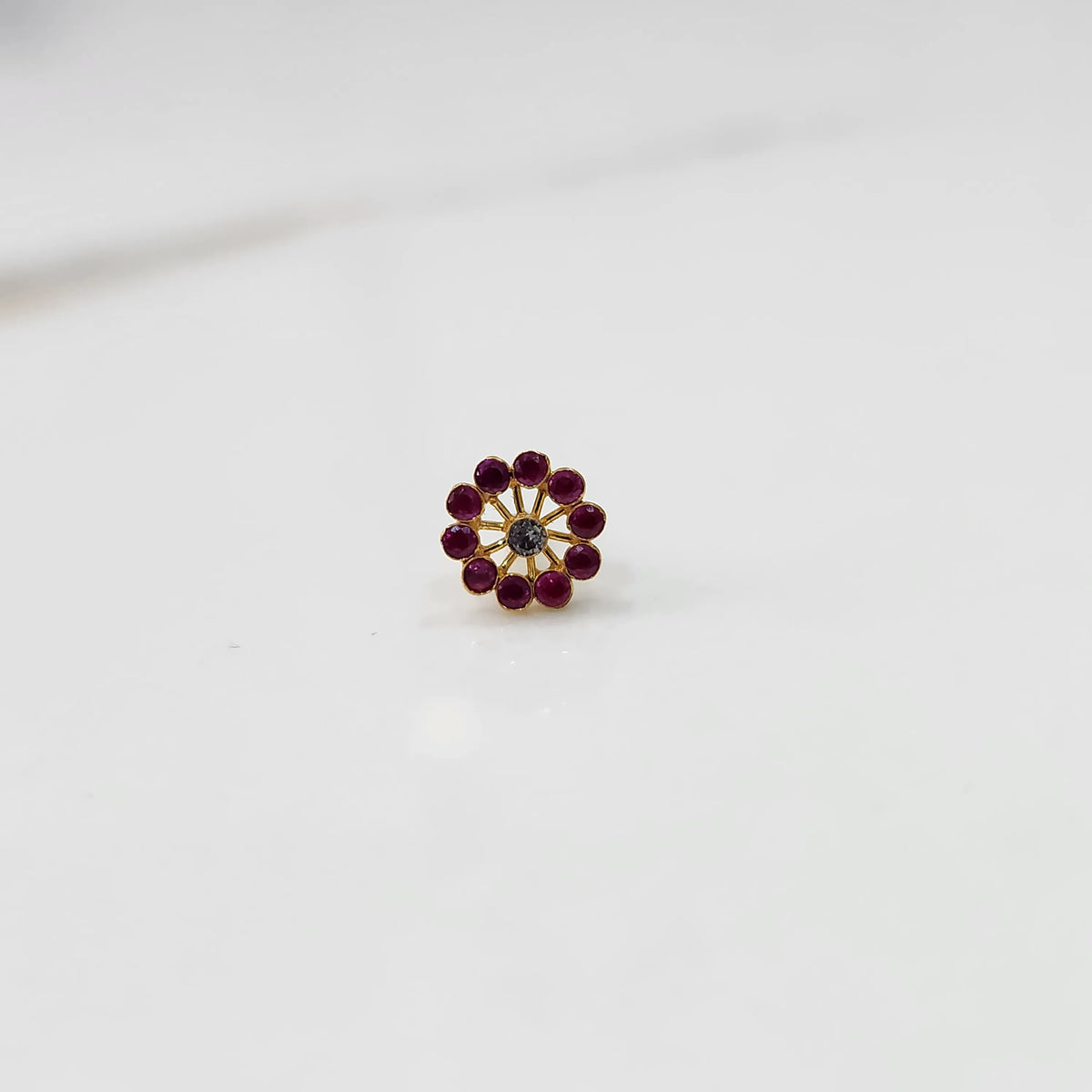 Front view of large gold nose pin with ruby-colored gemstone petals and clear center stone on white background