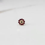 Front view of large gold nose pin with ruby-colored gemstone petals and clear center stone on white background
