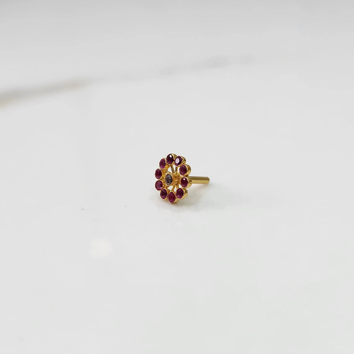 Large gold nose pin with ruby-colored gemstone petals and clear center stone on white background