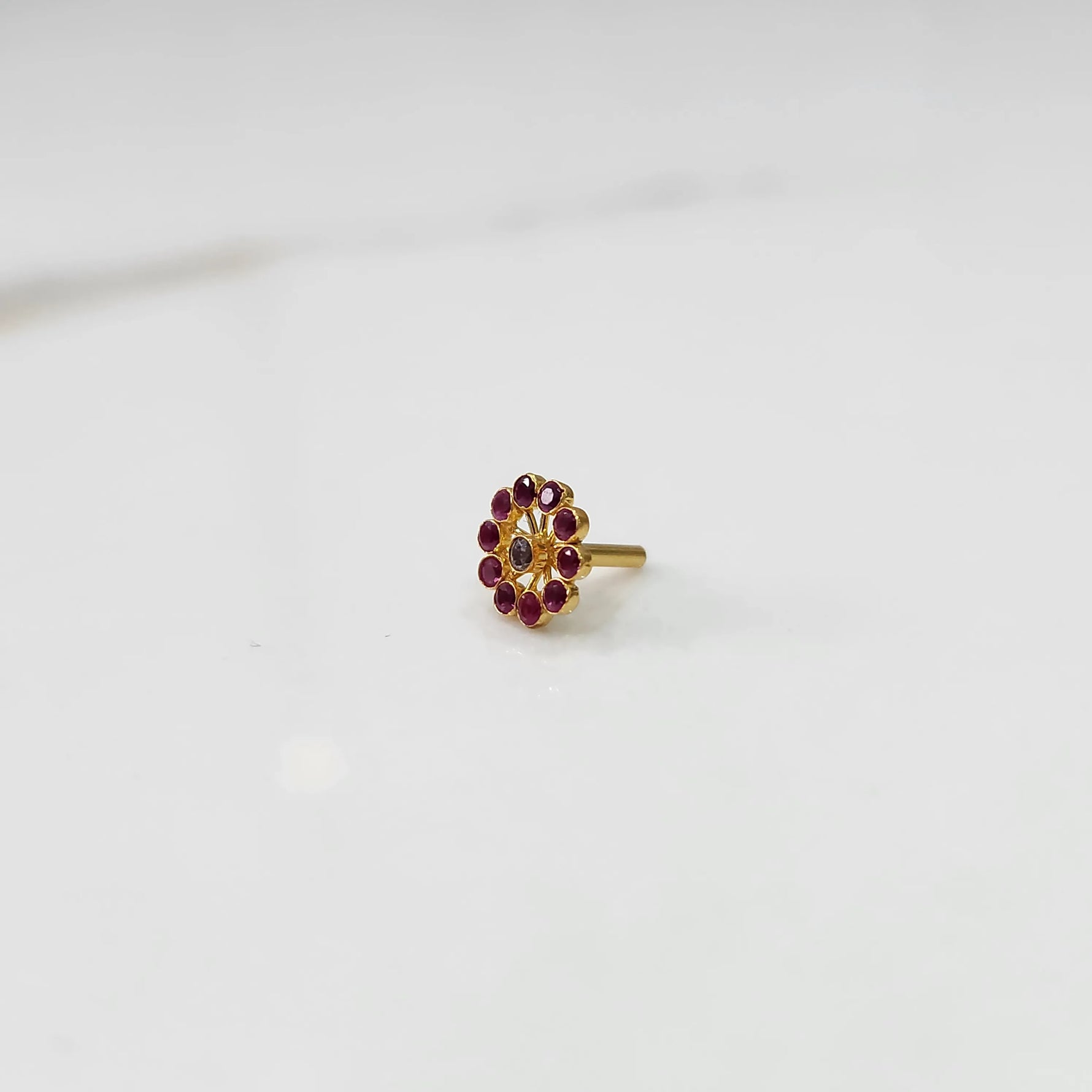 Large gold nose pin with ruby-colored gemstone petals and clear center stone on white background