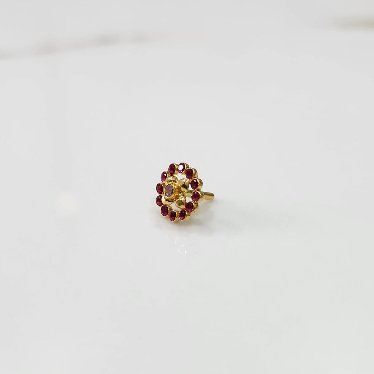 Gold floral nose pin with ruby-red stone halo, product shot
