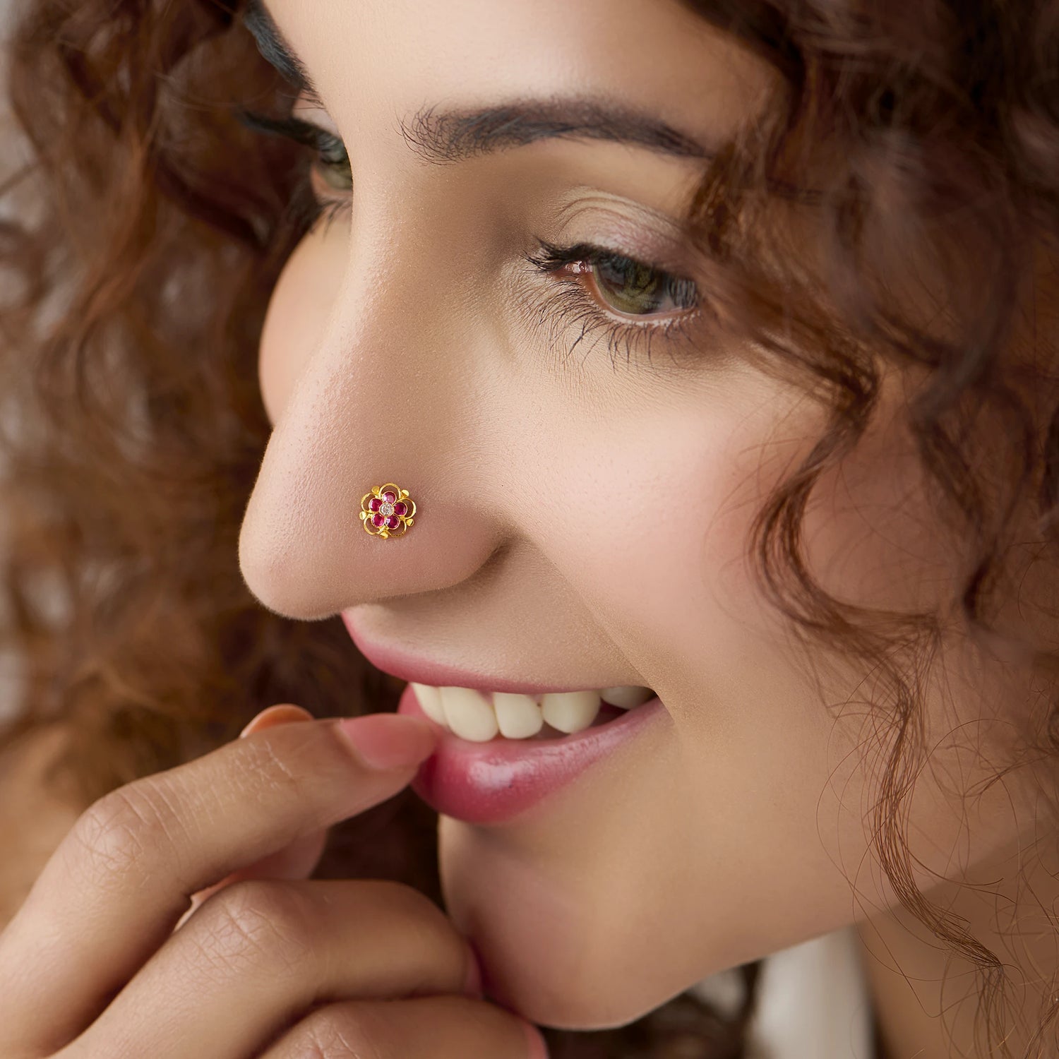 Woman wearing gold scalloped flower nose pin with pink stones