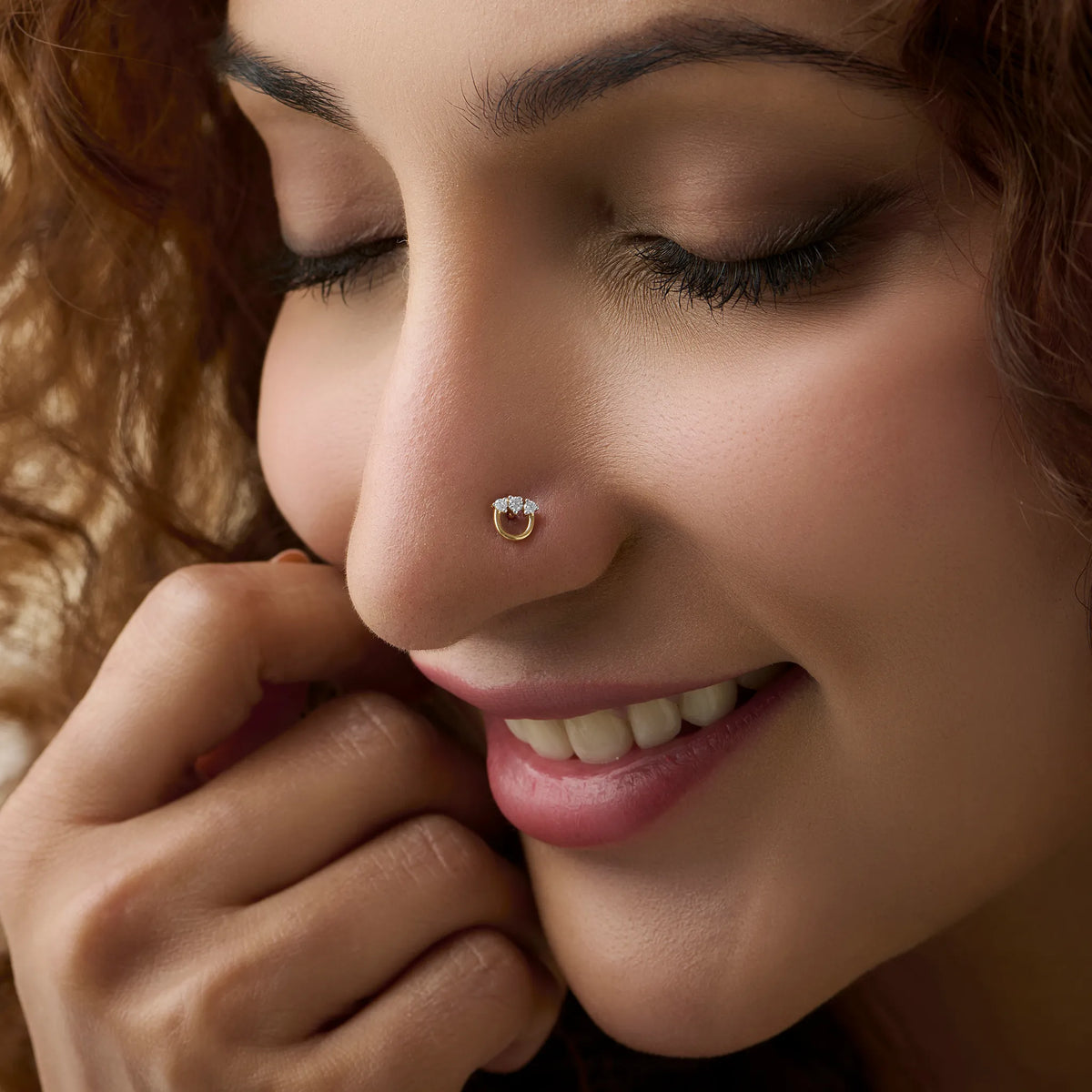 Smiling woman wearing a round gold nose pin with a shiny white stone.