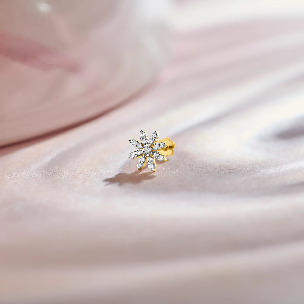 Gold snowflake-shaped stud with white stones on pink fabric