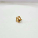 Gold nose pin with a star flower design and beaded border on a white surface