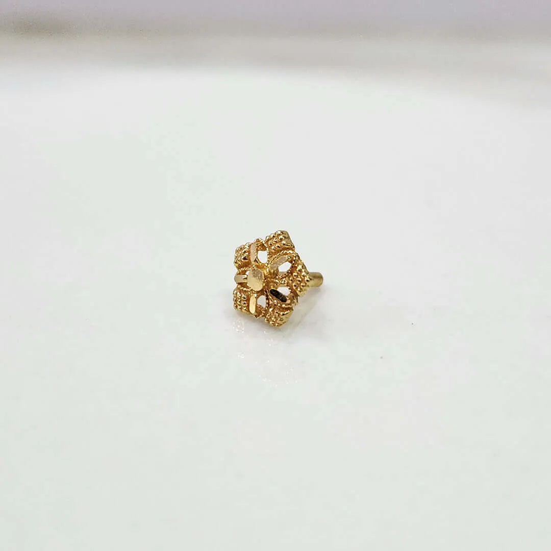 Gold nose pin with a star flower design and beaded border on a white surface
