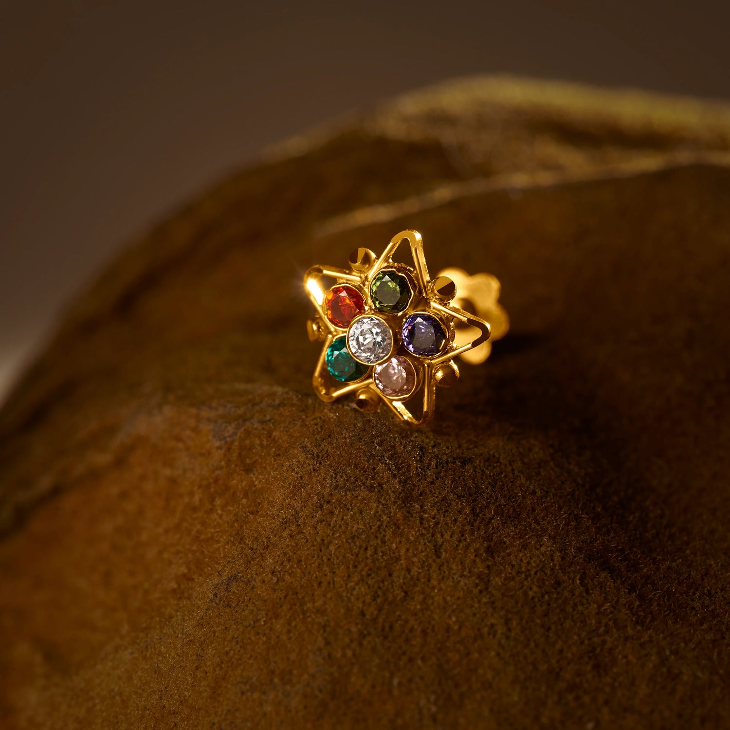 Nose pin design gold with multicolor floral gemstones on textured brown surface