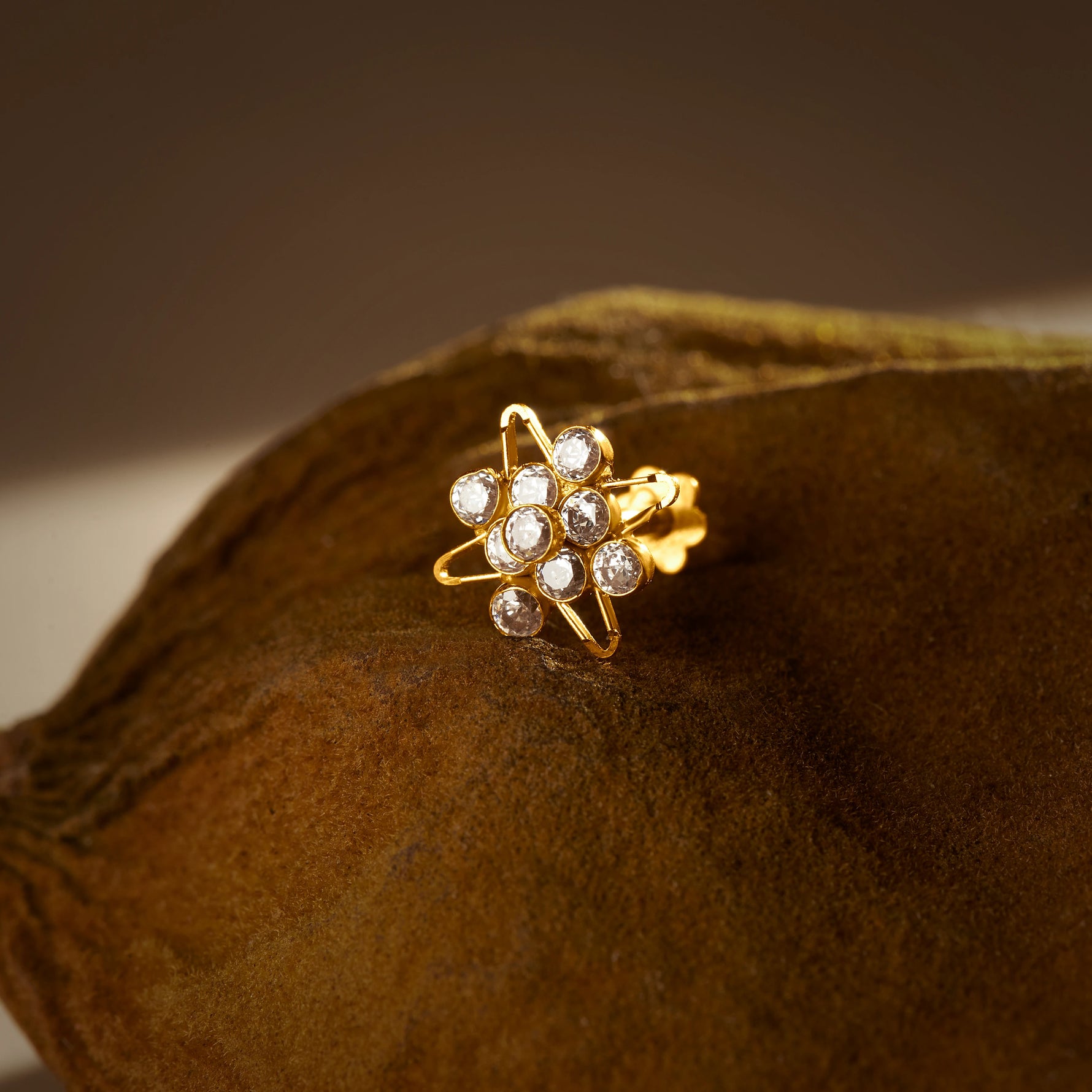 A gold star-outline stud earring with a cluster of round white stones at the center, placed on a textured brown fabric background