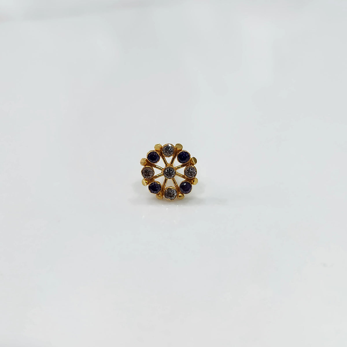 A gold star-frame stud earring with alternating purple and champagne-colored stones, placed on a white background
