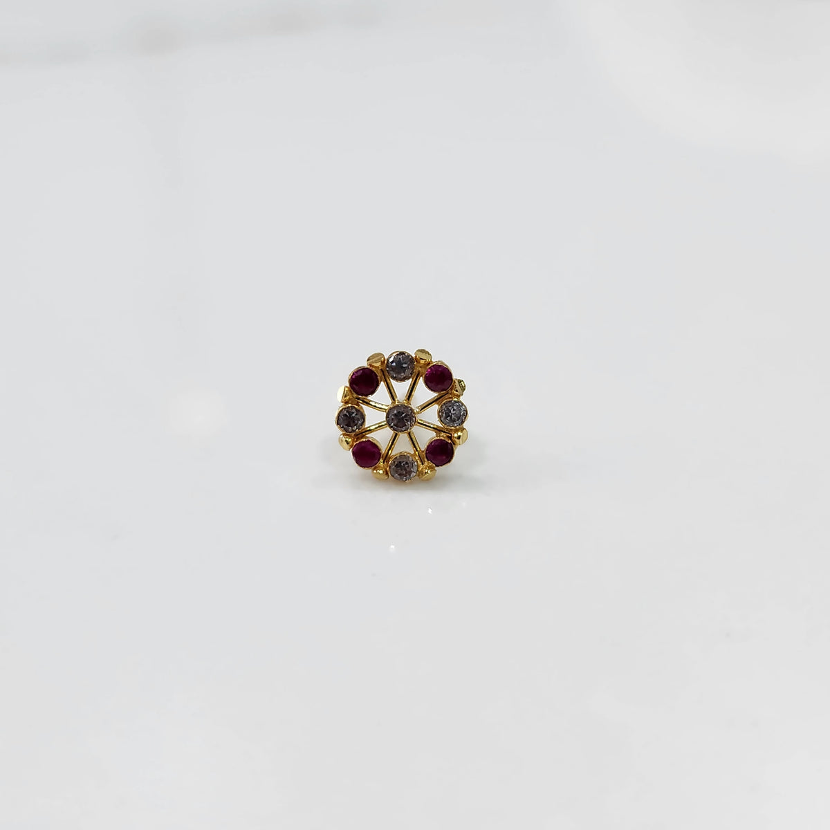 A gold star-frame stud earring with alternating red and grey stones, placed on a white background
