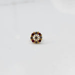 A gold star-frame stud earring with alternating red and grey stones, placed on a white background