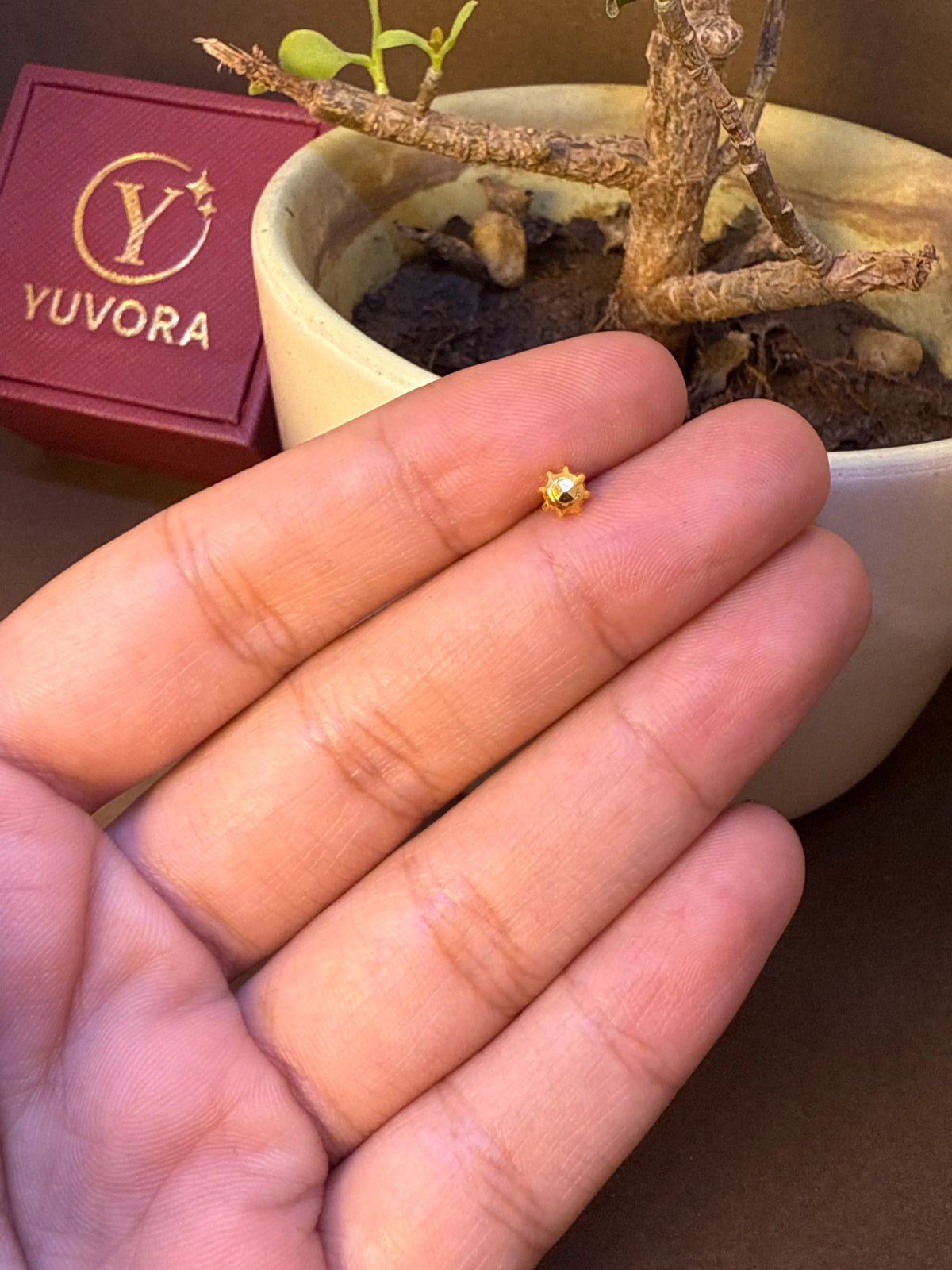 Small star-shaped gold nose pin with dark center stone, held in hand