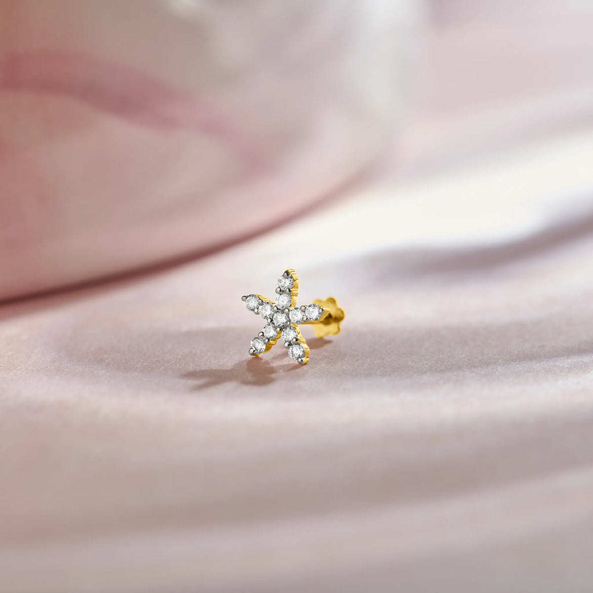 Nose pin of gold with star shaped diamond cluster design on soft pink fabric background