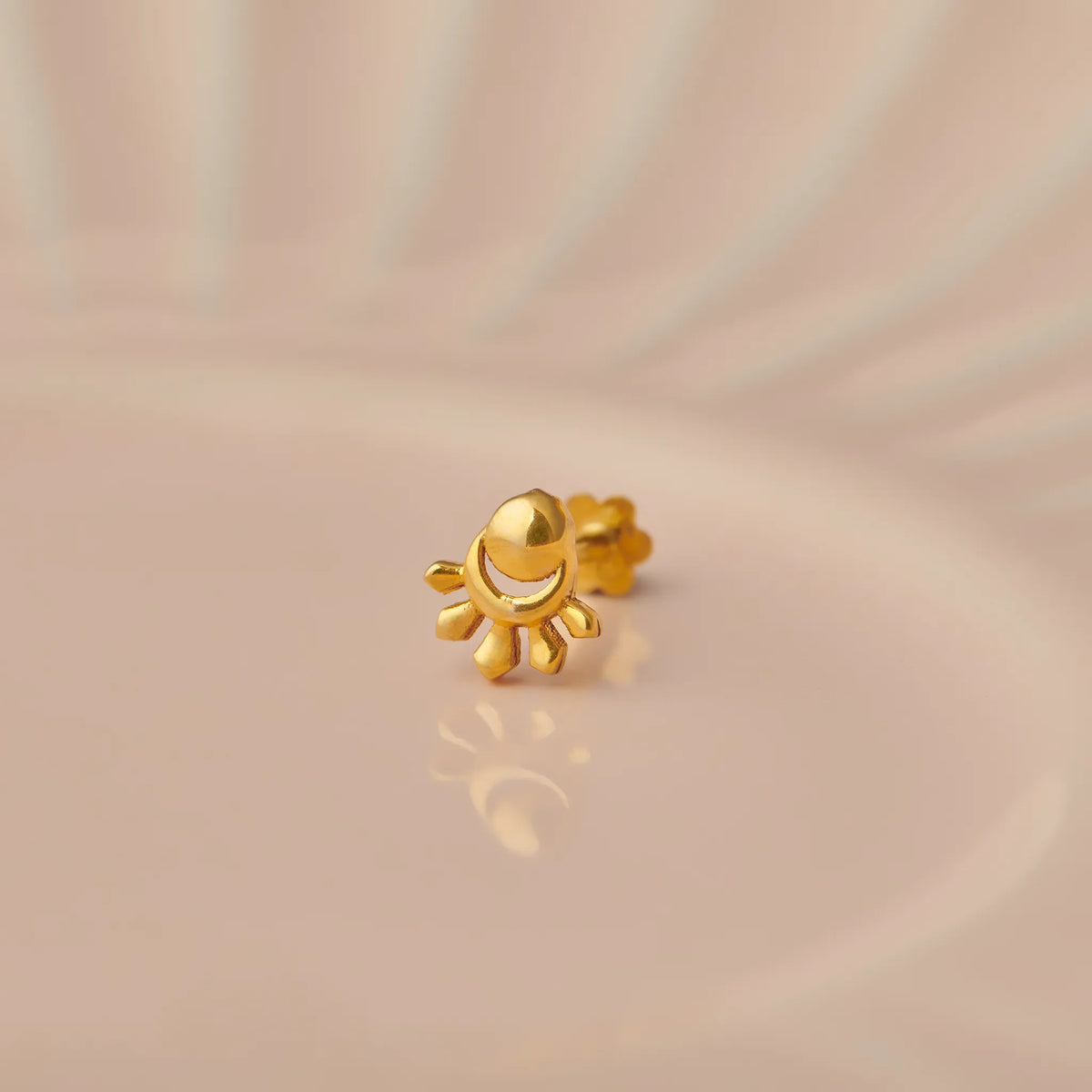 Gold sun flower-shaped nose stud with domed center on beige background