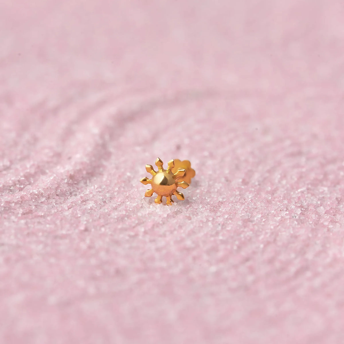 Gold sun-shaped nose stud with radiating rays on pink glitter background