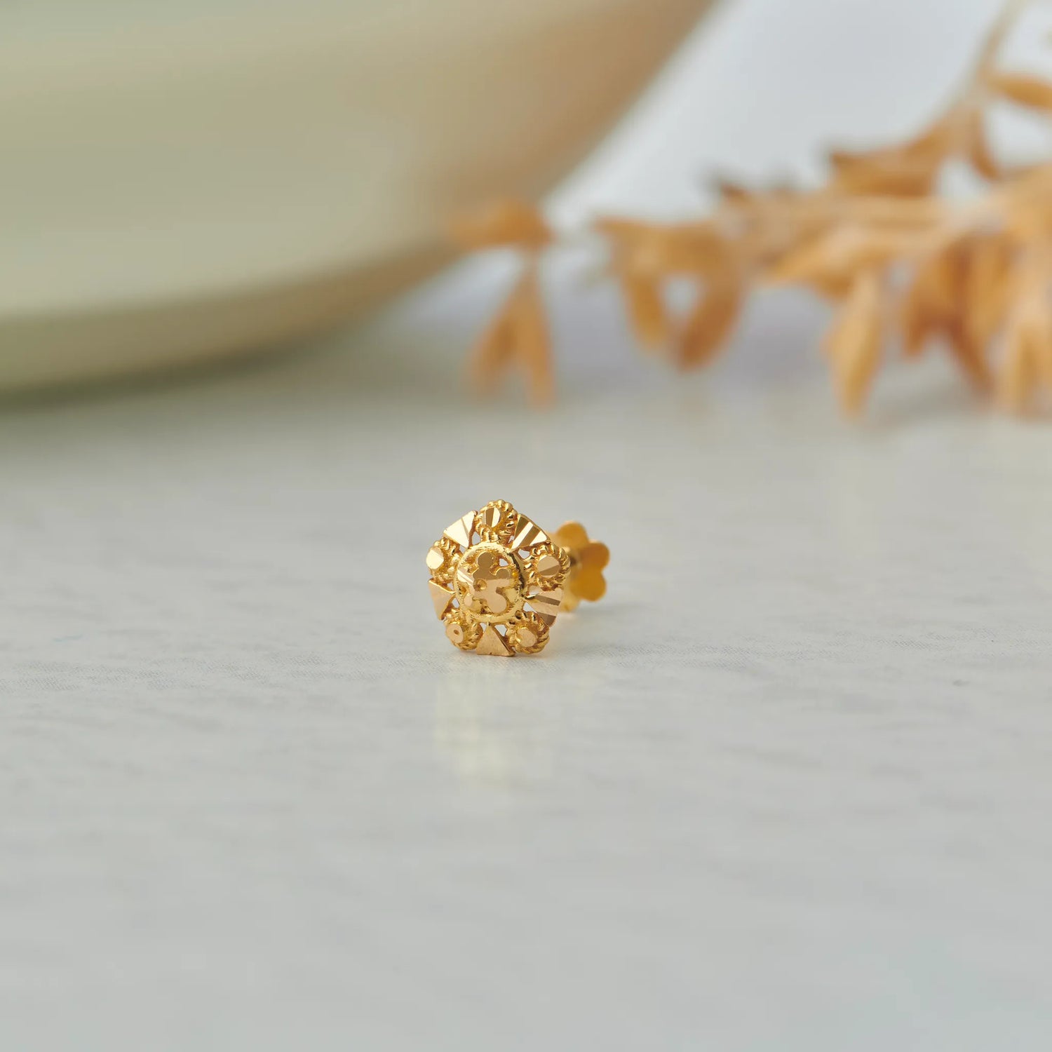 Gold flower-shaped stud earring with sunburst textured design