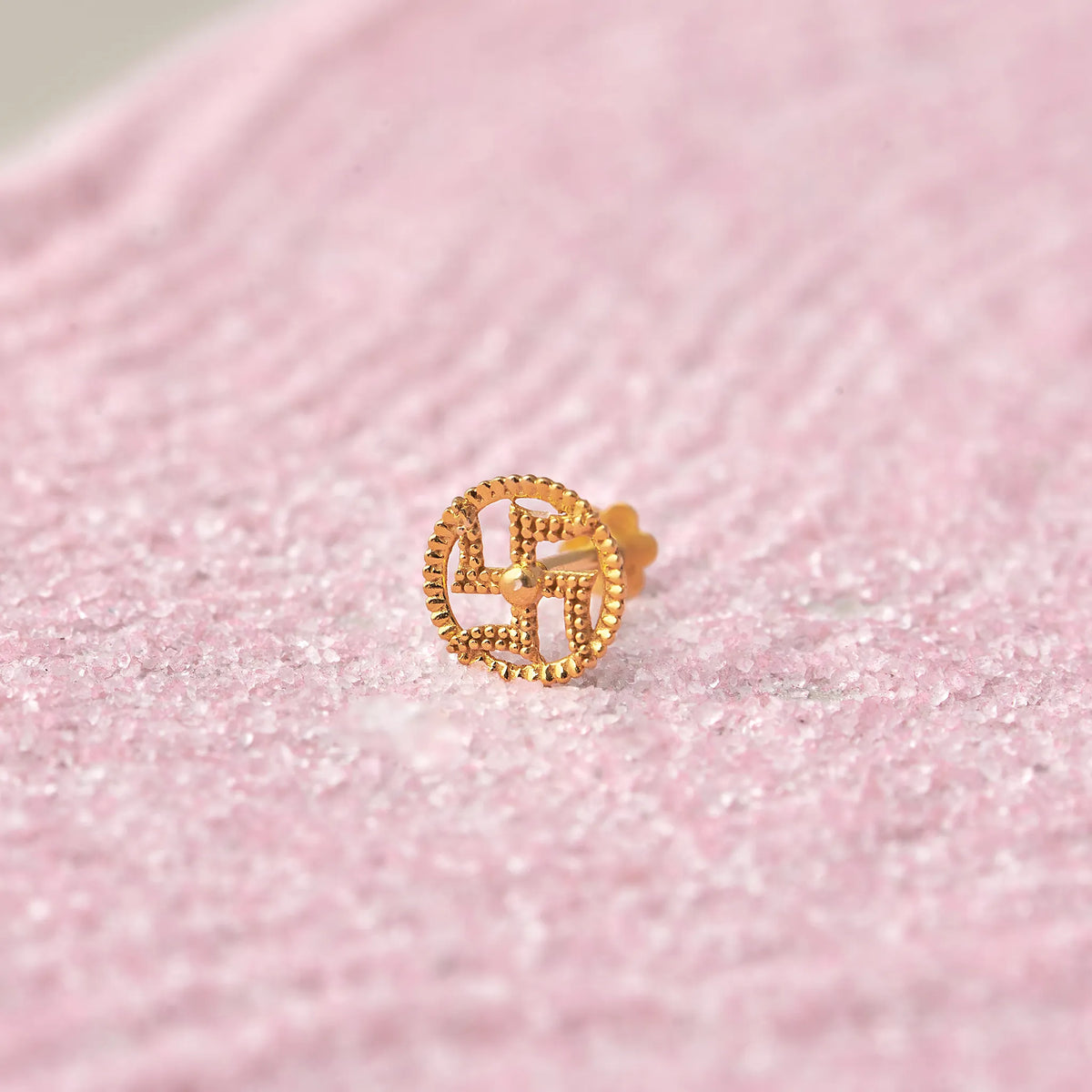 Gold swastik symbol in beaded circle nose stud on pink glitter background