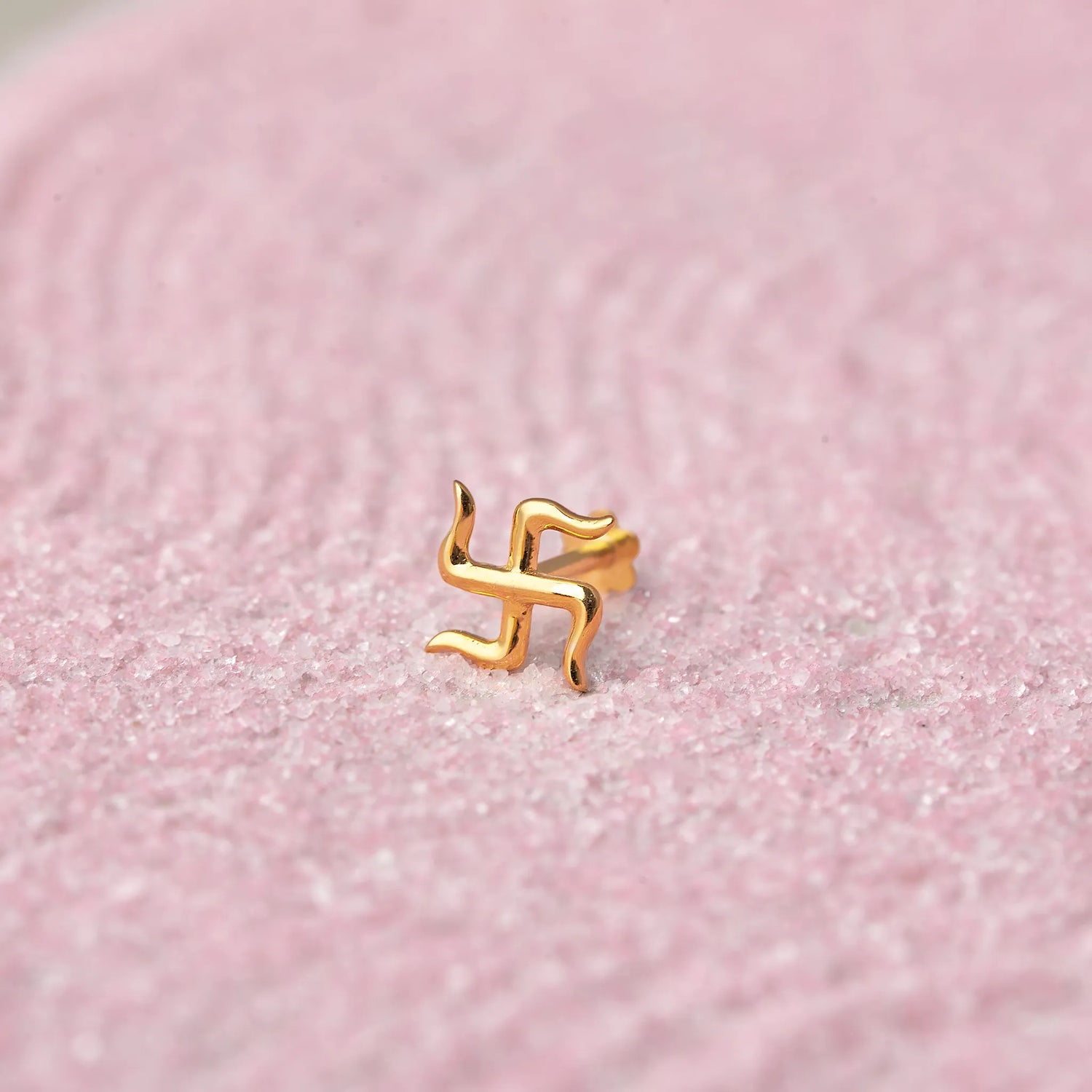 Gold swastik symbol nose stud on pink glitter background
