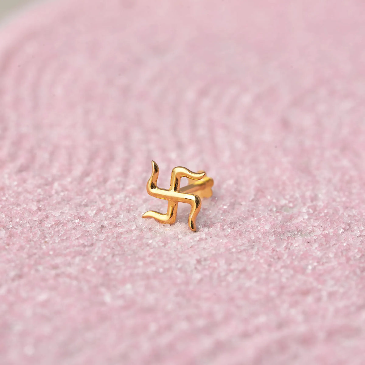 Gold swastik symbol nose stud on pink glitter background