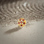 A gold swirl-design flower stud earring set with ruby and white stones, placed on a textured beige fabric background