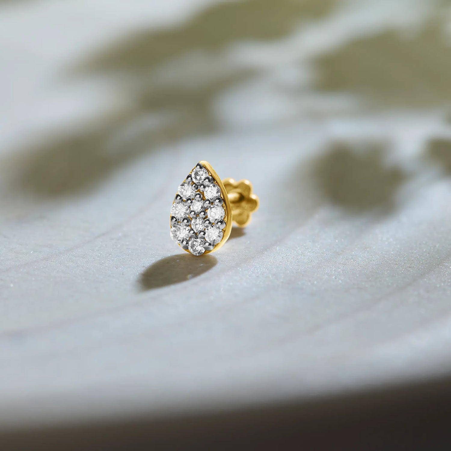 Teardrop cluster gold nose pins with sparkling diamonds on soft neutral background