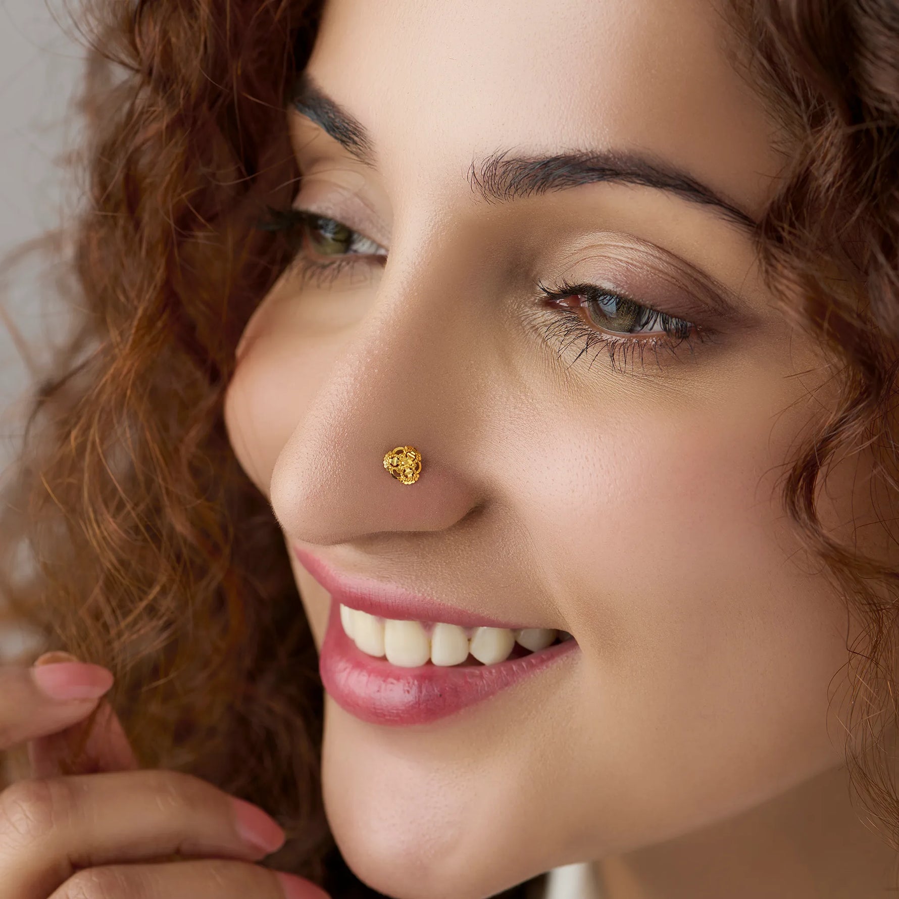 Close-up of a smiling woman with curly hair wearing a small textured gold nose pin