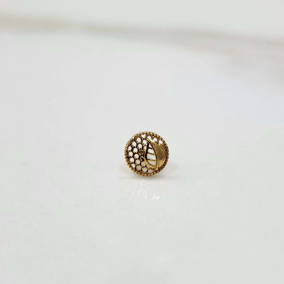 Close-up of a round gold nose stud with a textured net-like pattern