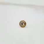 Close-up of a round gold nose stud with a textured net-like pattern
