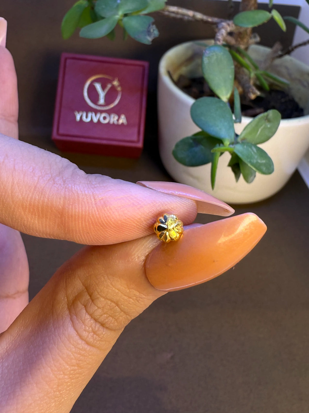 Gold textured nose stud held in fingers with Yuvora jewelry box in background