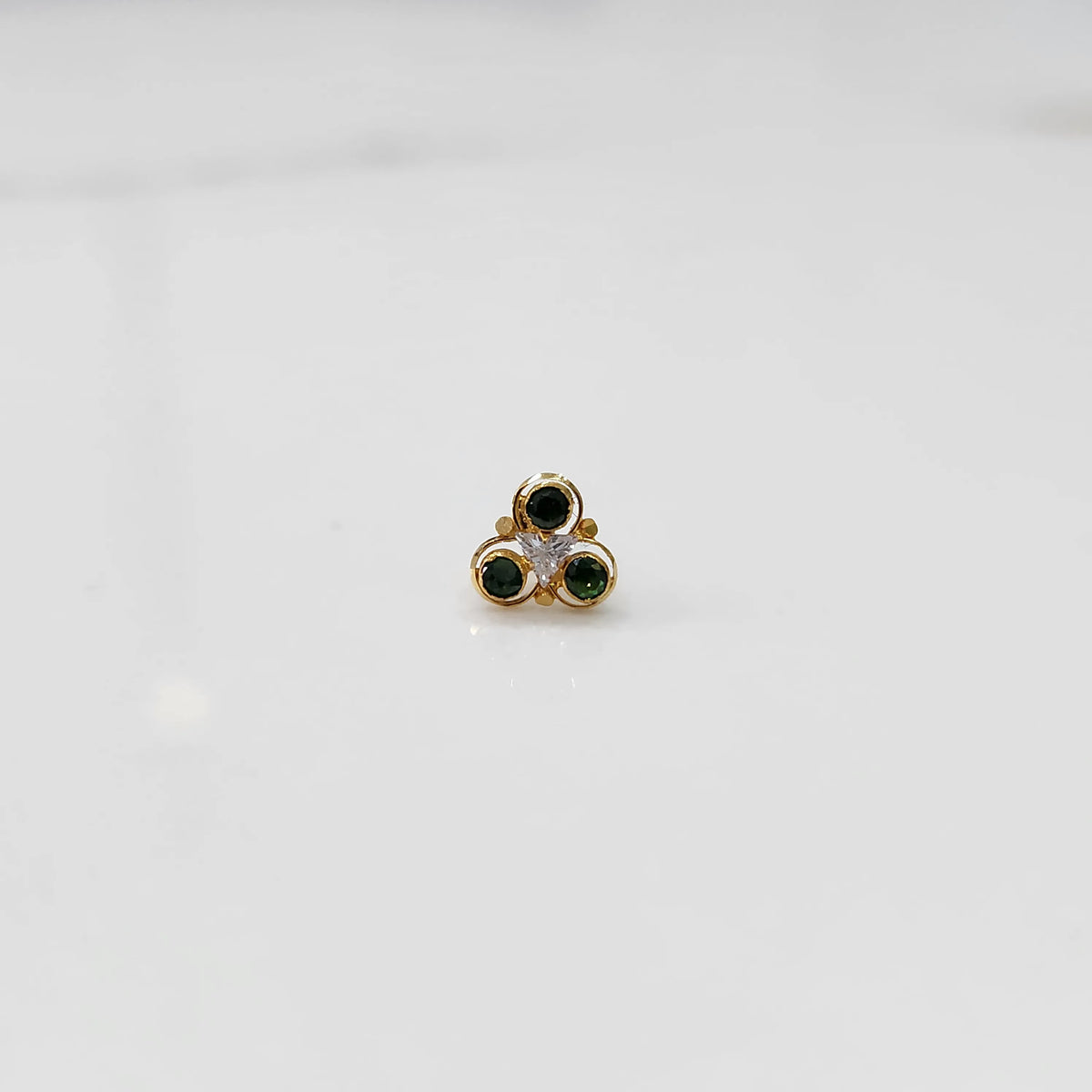 Close-up of gold three-stone ring featuring emerald and clear gemstones