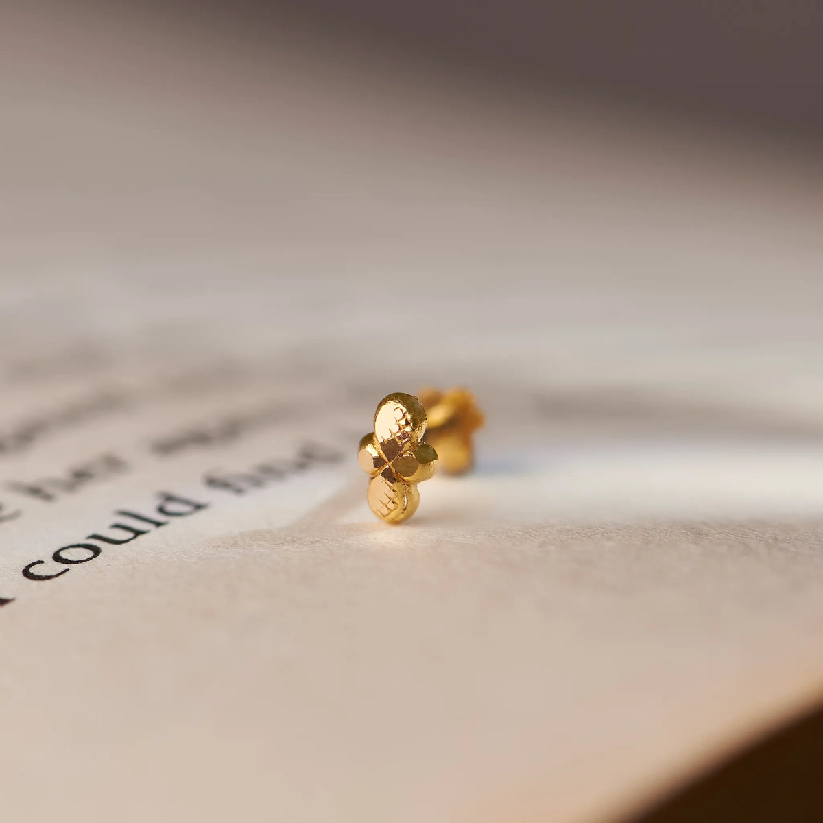 Close up of minimalist 18K gold nose pin placed on an open book page with soft natural lighting