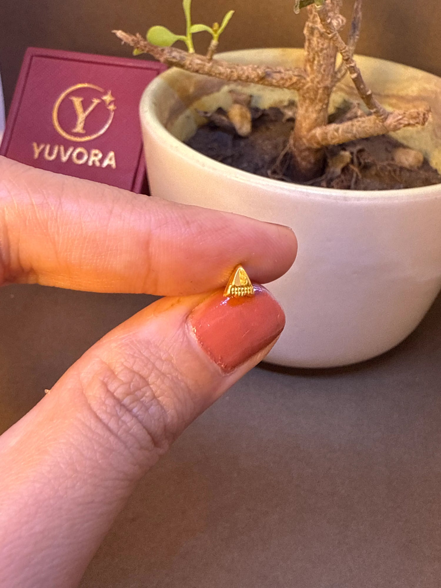 Small gold triangle-shaped nose pin stud with beaded edge held on fingertip