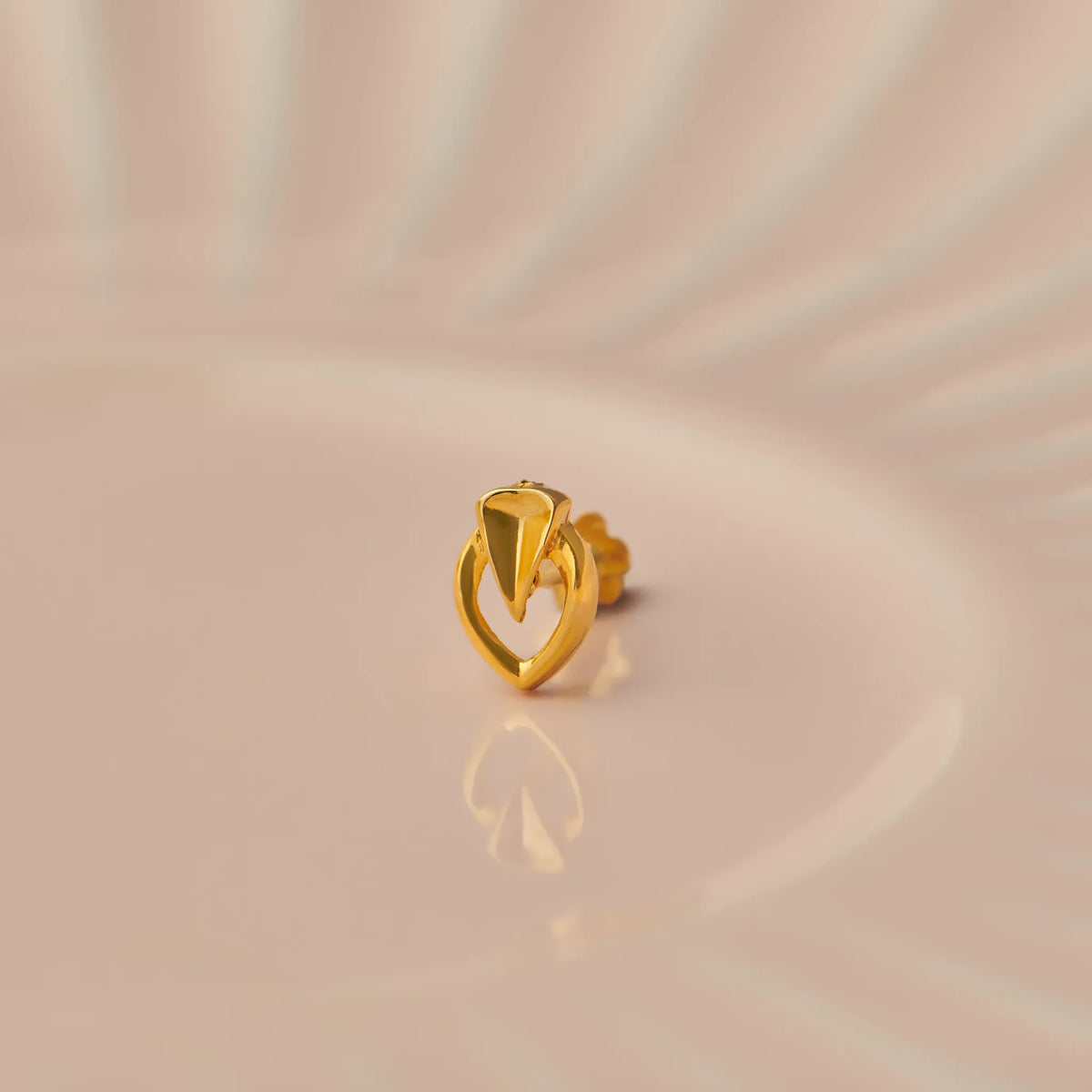 Gold nose stud with triangular stone in leaf-shaped setting on beige background