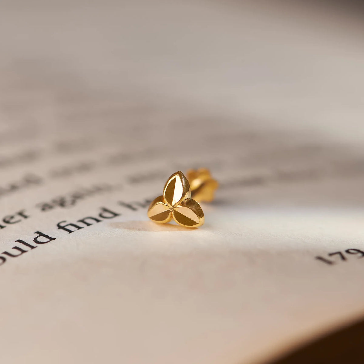 Simple gold nose pin design with three petal motif on book background